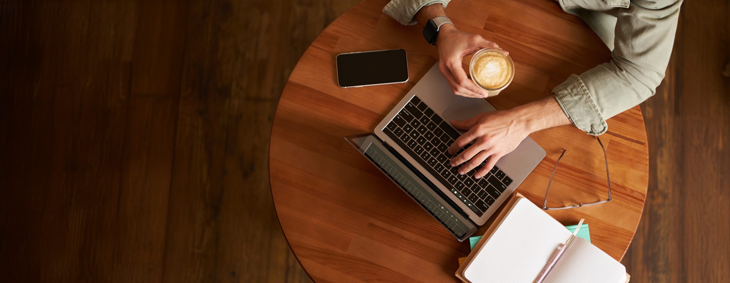 Co-working space, freelance and e-learning concept. Top view, male hands holding cup of coffee and using laptop. A man sitting in cafe and working or studying online.